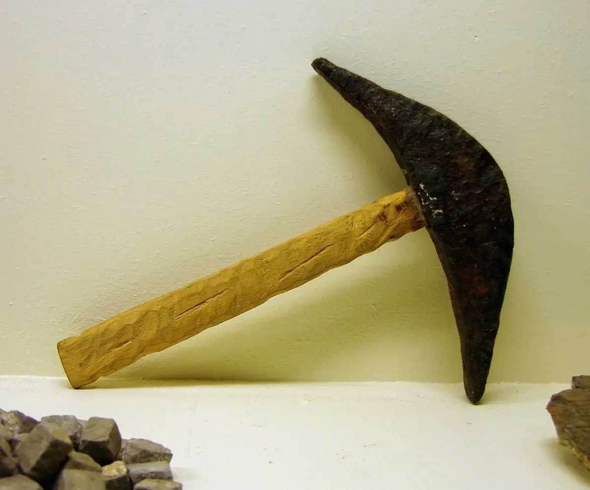 Ancien marteau de tailleur de pierre à manche de bois, posé contre un mur clair
