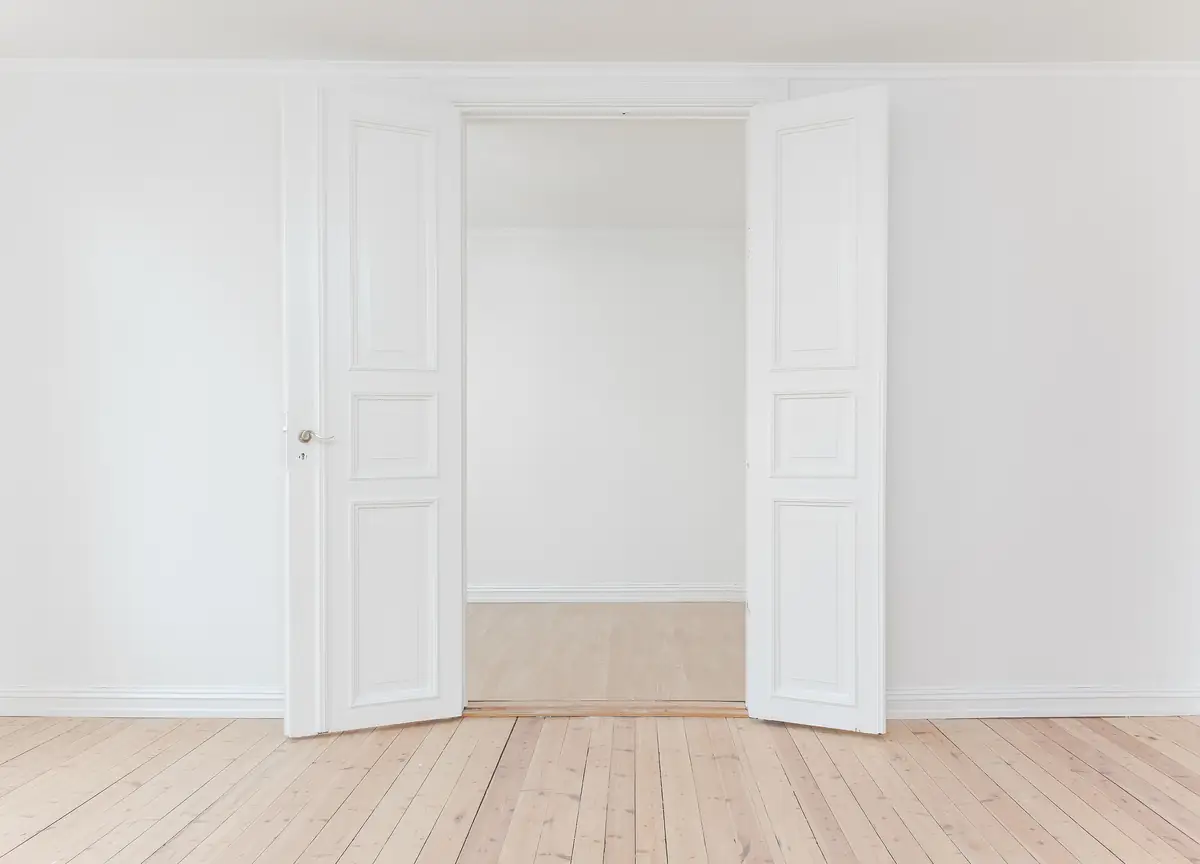 Pièce aux murs blancs, double porte à moulures ouverte et parquet clair