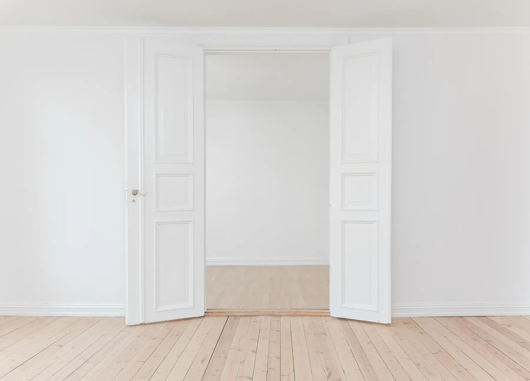 Pièce aux murs blancs, double porte à moulures ouverte et parquet clair